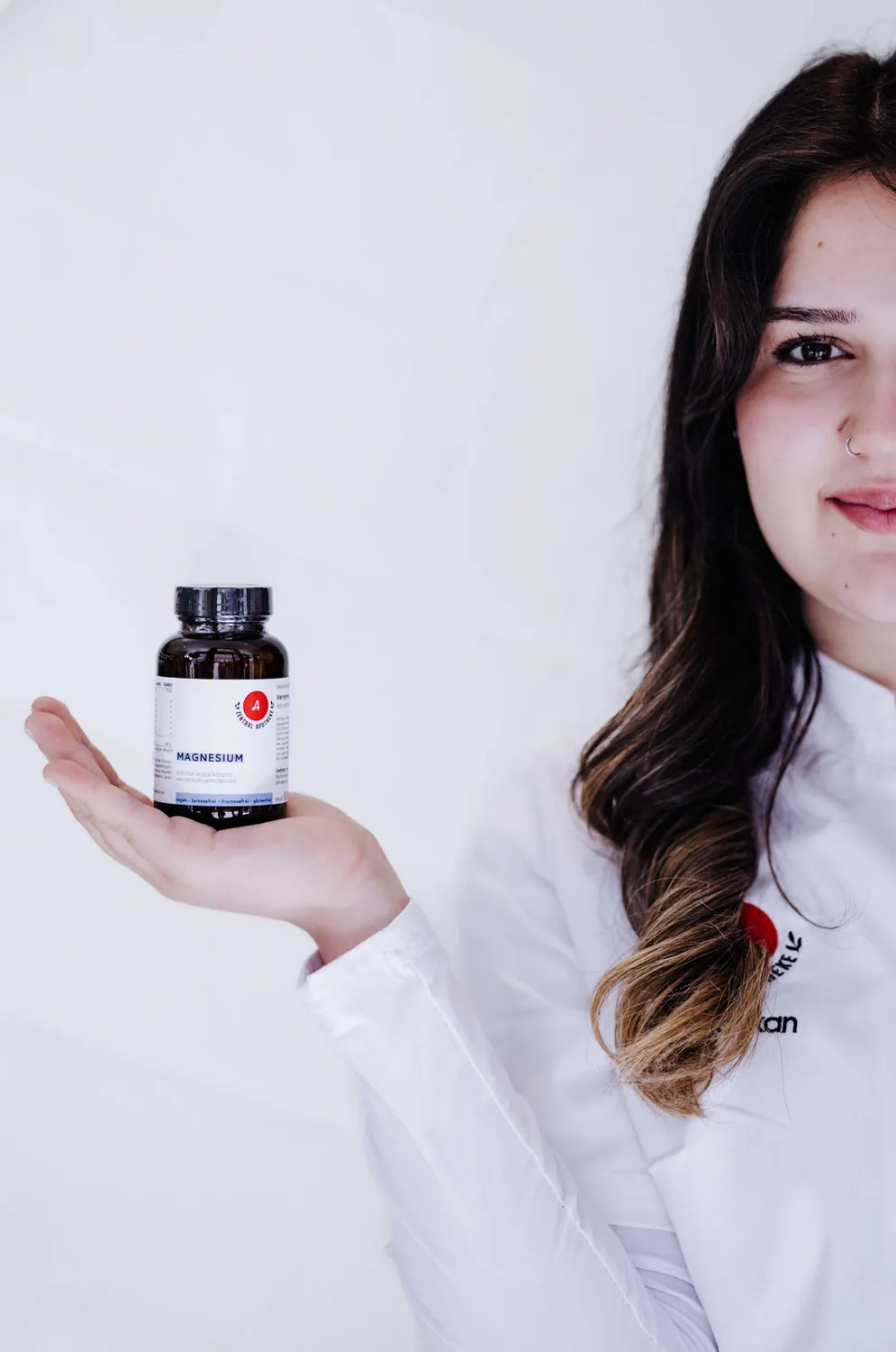 Mitarbeiterin hält eine Dose Magnesium der Eigenmarke auf der ausgestreckten Hand, heller Hintergrund