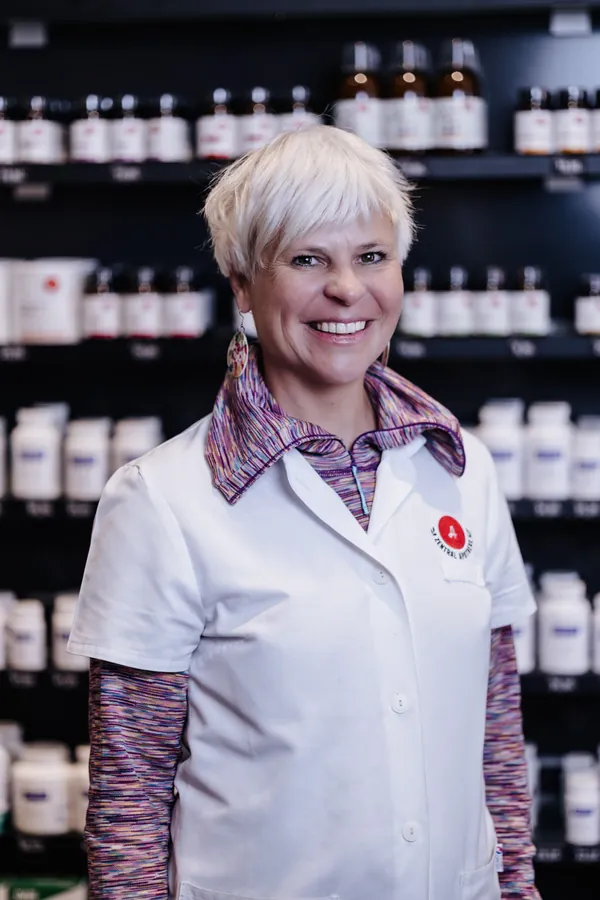 Porträt von Evelyn Rützler im weißen Kittel vor dem Apothekenregal