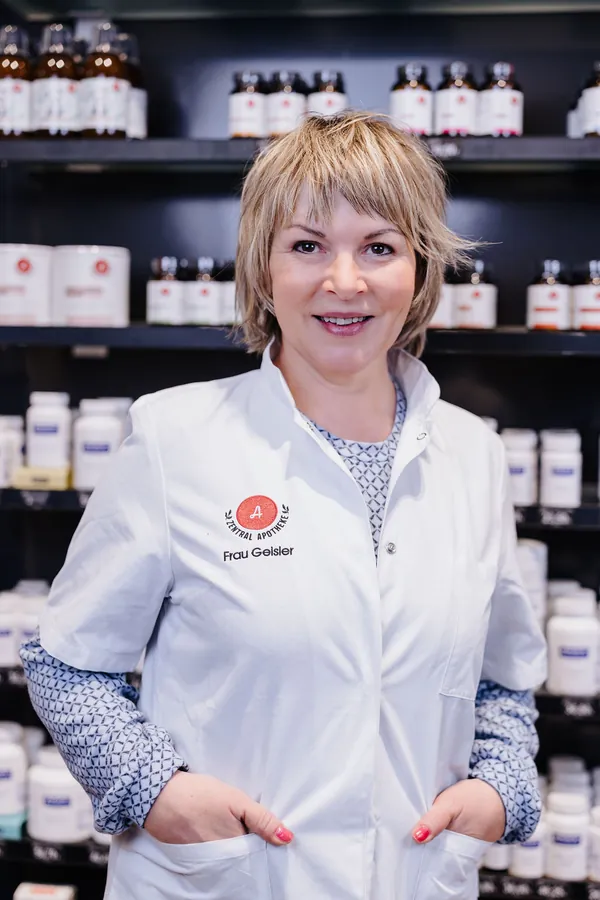 Porträt von Karin Wieser im weißen Kittel vor dem Apothekenregal