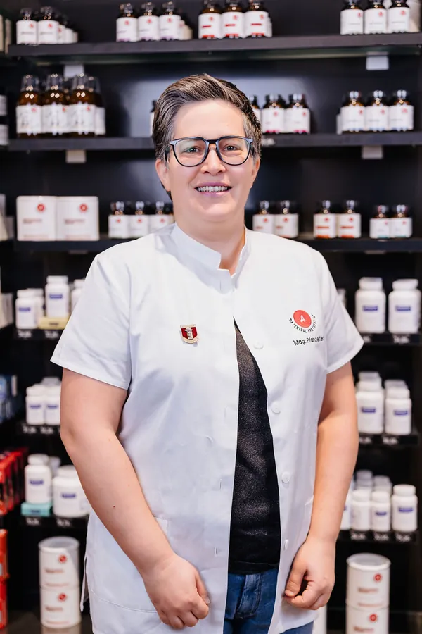 Porträt von Katherina Pfanzelter im weißen Kittel vor dem Apothekenregal