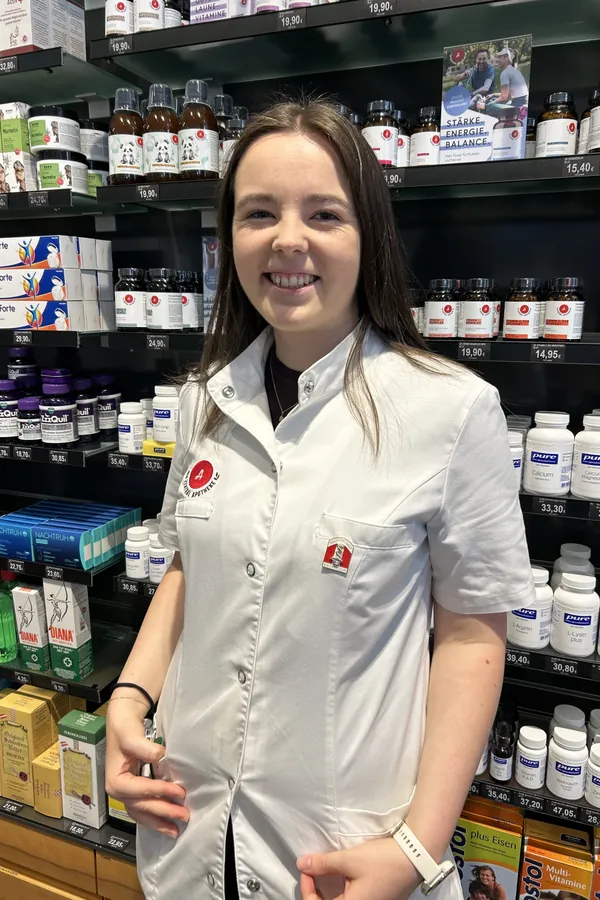 Porträt von Katja Silbernagl im weißen Kittel vor dem Apothekenregal