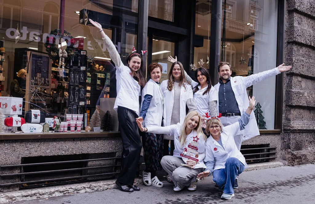 Das Team der Zentral-Apotheke winkt vor dem weihnachtlich dekorierten Schaufenster